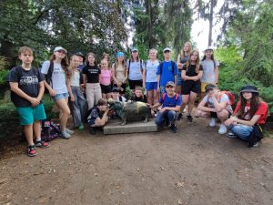 Uczniowie biorący udział w wycieczce pozują do wspólnego zdjęcia przy mosiężnym posągu hipopotama w otoczeniu drzew.