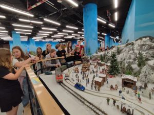 Uczniowie stoją przy makiecie z kolejką jeżdżącą wokół zasypanej śniegiem góry.