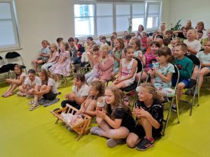 Uczniowie klas 0- III oglądający przedstawienie klaszczą. W pierwszym rzędzie siedzą na podłodze dziewczynki a przed nimi stoi kołyska z lalką.