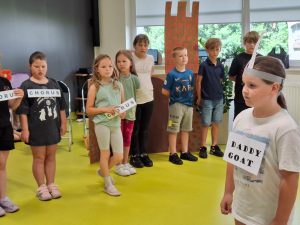 Na pierwszym planie widoczna jest stojąca bokiem uczennica klasy 2 w papierowej opasce z uszami i przytwierdzoną do koszulki tabliczką z napisem "daddy goat". W tle widać stojących w rzędzie innych uczniów. Część z nich trzyma lub ma przyczepione do koszulki tabliczki z angielskimi słówkami.