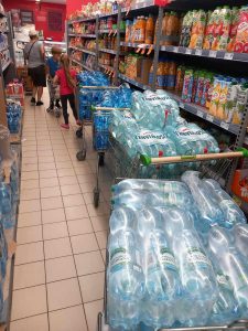 Zdjęcie trzech wózków sklepowych wyładowanych butelkami z wodą mineralną. Wóżki stoją w rzędzie w alejce sklepowej.