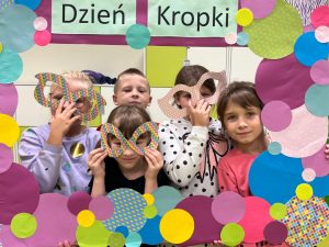 Pięcioro uczniów pozuje do zdjęcia w dużej ramie utworzonej z kolorowych kropek różnej wielkości. Troje uczniów trzyma na wysokości oczu duże kolorowe okulary wycięte z kartonu.