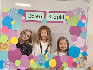 Trzy dziewczynki pozują do zdjęcia trzymają w dłoniach dużą ramkę utworzoną z różnej wielkości kolorowych kół. Na górze ramy widnieje napis "Dzień Kropki".