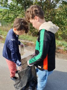 Dwóch uczniów trzyma czarny worek na śmieci. Jeden z z chłopców w drugiej dłoni trzyma plastikową butelkę.