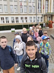 Uczniowie stoją w parach tworząc rząd na placu przed urzędem w Toruniu. Uczeń widoczny na pierwszym planie patrzy wprost w obiektyw aparatu.