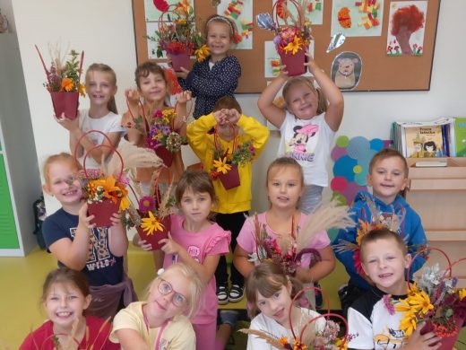 Uczniowie klasy pierwszej pozują do wspólnego zdjęcia z wykonanymi przez siebie jesiennymi koszykami. Dzieci szeroko się uśmiechają i z duma prezentują swoje prace.