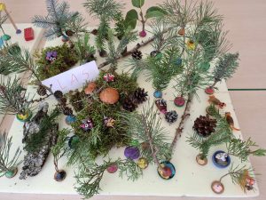 Zdjęcie przygotowanych przez uczniów dekoracji z darów jesieni łączonych ze sobą za pomocą plasteliny. Pomiędzy gałązkami widoczna jest biała kartka z odręcznym napisem "LAS".