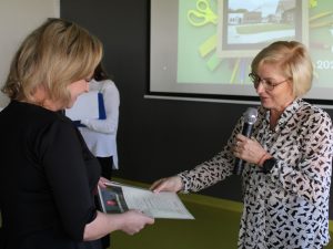 Pani dyrektor wręcza stojącej na przeciwko sekretarz szkoły dyplom.