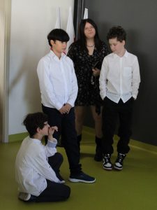 Na zdjęciu widocznych jest czworo uczniów klasy VI . Troje z nich stoi - pomiędzy dwoma chłopcami w białych koszulach i czarnuch spodniach stoi uczennica w ciemnej sukience. Z przodu czwarty uczeń klęka na podłodze.