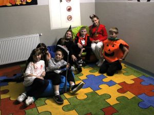 Siedmioro uczniów klasy czwartej pozuje do wspólnego zdjęcia siedząc na pufach ustawionych na kolorowym dywanie. Uczniowie mają na sobie halołinowe przebrania.