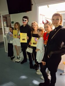 Uczniowie nagrodzeni w konkursie za najlepsze przebrania stoją w jednym rzędzie wraz z przedstawicielami samorządu uczniowskiego. Nagrodzeni uczniowie trzymają przed sobą dyplomy.