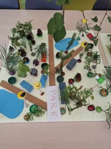 Zdjęcia kartki papiery z napisem "PARK" ozdobionej gałązkami drzew iglastych oraz liściastych, małymi szyszkami oraz elementami wyciętym z kolorowego papieru tak, by cała p-raca imitowała park.