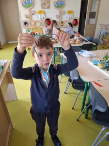 Uczeń oddziału przedszkolnego pozuje do zdjęcia trzymając w dłoniach wyciągniętych na wysokość głowy otrzymany medal z okazji dnia chłopaka.