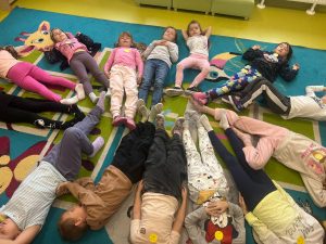 Uczniowie świetlicy leżą na dywanie tworząc koło i stykając się w jego środku wyciągniętymi stopami.