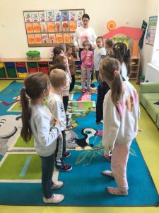 Uczniowie przebywający na świetlicy stoją na dywanie w dwóch rzędach ustawionych naprzeciwko siebie. Na końcu pomiędzy nimi stoi wychowawczyni a przed nią jedna z dziewczynek.