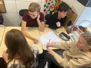 Uczniowie przebywający na świetlicy siedzą przy wspólnym stole i tworzą plakat z okazji Światowego Dnia Zdrowia Psychicznego. Jeden z chłopców patrzy w stronę okna i opiera dłonie o stół.