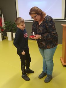 Uczeń stoi przy kobiecie prowadzącej prelekcje. Razem z panią patrzy na czerwone urządzenie z ustnikiem, które kobieta trzyma w dłoniach.