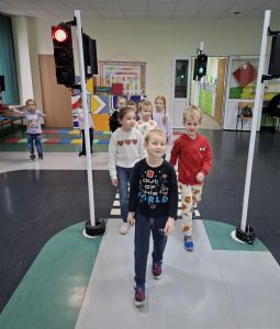 Uczniowie oddziału przedszkolnego idą na wprost siebie przechodząc przez pasy narysowane na podłodze sali w toruńskim oddziale WORD. Na pierwszym planie widać uśmiechniętego chłopca stawiającego duże kroki.