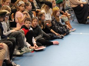Zdjęcie uczniów uczestniczących w apelu. Na pierwszym planie widoczna jest dwójka uczniów patrząca bezpośrednio w stronę obiektywu. Pozostałe dzieci patrzą przed siebie.