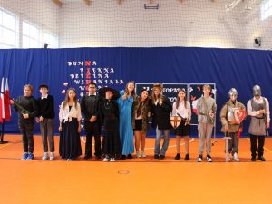 Uczniowie klasy siódmej pozują do wspólnego zdjęcia stojąc w jednym rzędzie. Dzieci ubrane są w różnorodne stroje postaci historycznych.