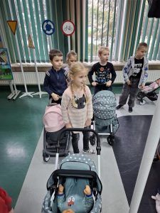 Uczniowie oddziału przedszkolnego stoją na szarej ścieżce namalowanej na podłodze sali toruńskiego oddziału WORD. Dzieci pchają przed sobą wózki dla lalek.
