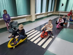 Uczniowie oddziału przedszkolnego jeżdżą kolorowymi pojazdami na kółkach po sali toruńskiego oddziału WORD. Dzieci przejeżdżają przez namalowane na podłodze pasy.
