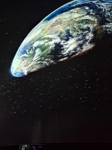 Zdjęcie obrazu wyświetlanego w kopule, przedstawiającego fragment Ziemi widocznej z kosmosu oraz gwiazd ją otaczających.