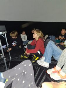 Uczniowie siedzą w kopule i oglądają wyświetlany seans filmowy.