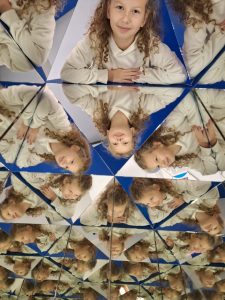 Zdjęcie przedstawia odbicie uczennicy w pryzmatach ustawionych obok siebie.