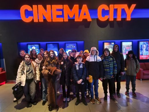 Uczniowie klasy VII pozują do wspólnego zdjęcia na korytarzu kina. Nad nimi widoczny jest pomarańczowy napis "CINEMA CITY".