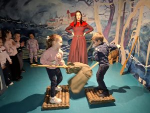 Oddział przedszkolny w "domu Legend". Dwoje uczniów stoi na przeciwko siebie na drewnianych podkładkach ustawionych na krótkich belkach. Oboje trzymają tyczki na końcach których zawieszone są worki wypełnione pierzem i walczą na nie krzyżujące je przed sobą. Z tyłu stoi kobieta podpierająca swoje dłonie o biodra.