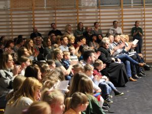 Zdjęcie widowni oklaskującej występ uczniów w jasełkach szkolnych.