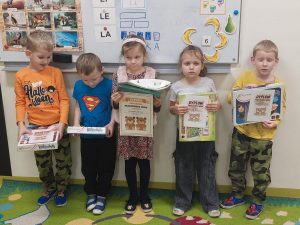 Pięcioro uczniów stoi pod tablicą na dywanie w sali lekcyjnej. Dzieci trzymają przed sobą otrzymane dyplomy i nagrody.