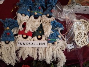 Zdjęcie przygotowanych do sprzedaży ozdób wykonanych przez uczniów z włóczki. Na ułożonych obok siebie ozdobach leży karteczka z napisem "MIKOŁAJ - 10 zł".