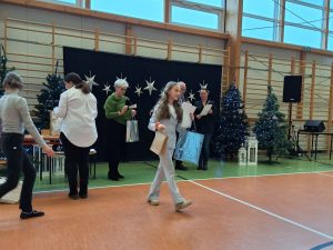 Uczennica po odebraniu nagród odchodzi trzymając w dłoniach dwie papierowy torby oraz dyplom. Za nią stoją przedstawiciele jury wręczający nagrody.