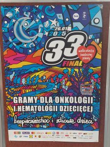 Zdjęcie plakatu Wielkiej orkiestry świątecznej pomocy - na tle grafiki w kolorze niebieskim z akcentami w kolorach żółtym, pomarańczowym i czerwonym widnieje biały napis "26.01.2025 33 finał" a obok niego czerwone serduszko z napisem "wielka orkiestra świątecznej pomocy". Poniżej biały napis: "GRAMY DLA ONKOLOGII I METALOGII DZIECIĘCEJ" i poniżej kolejny "bezpieczeństwo i zdrowie dzieci". U doły widać logo patronów medialnych akcji.