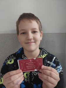 Uśmiechnięty uczeń stoi przy ścianie trzymając przed sobą wygrany los z napisem "Herbata z Panią Dyrektor (klasa 8)".