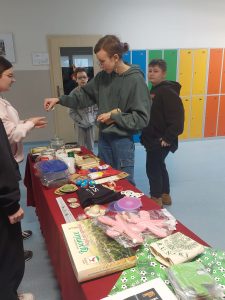 Uczniowie klasy szóstej stoją przy stoisku z fantami. jedna z dziewczynek przekazuje koleżance stojącej po drugiej stronie stołu pieniądze.