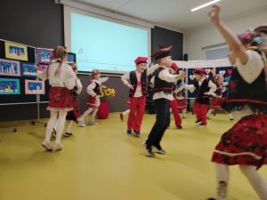 Uczniowie oddziału przedszkolnego w strojach krakowiaków tańczą na sali teatralnej.