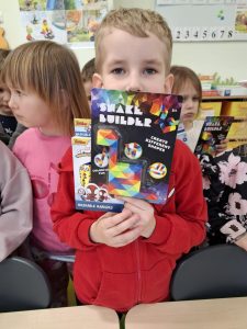 Uczeń pozuje do zdjęcia trzymając na wysokości twarzy otrzymane w konkursie dwie nagrody w kształcie prostokątów.