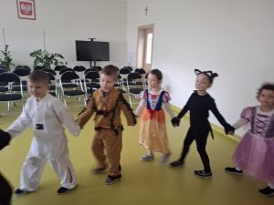 Uczniowie tańczą tworząc długiego węża, na sali gimnastycznej. Uczestnicy zabawy trzymają się za dłonie.