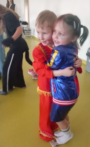 Dwoje uczniów ubranych w swoje przebrania karnawałowe mocno się przytula obejmując dłońmi i stojąc na zwiniętym kawałku gazety.