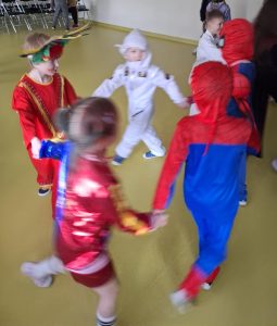 Uczniowie w swoich przebraniach tańczą na balu trzymając się za dłonie i formułując swoimi ciałami małe kółko.