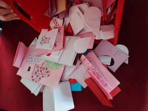 Zdjęcie wysypujących się z czerwonego pudełka karteczek walentynkowych o różnych kształtach i rozmiarach.