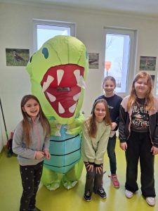 Cztery uczennice pozują do wspólnego zdjęcia z osoba przebraną na dinozaura.