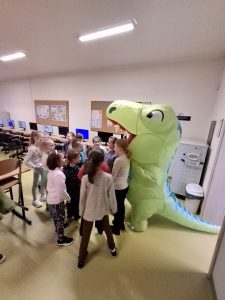 Uczniowie klasy drugiej stoją w grupie przed osobą przebrana w strój dinozaura.