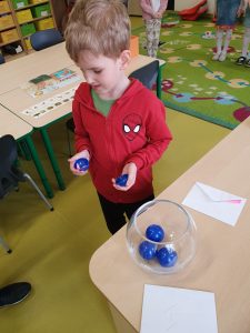 Uczeń oddziału przedszkolnego trzyma w dłoniach przed sobą dwie połówki niebieskiej kuli. Chłopiec spogląda w ich kierunku.