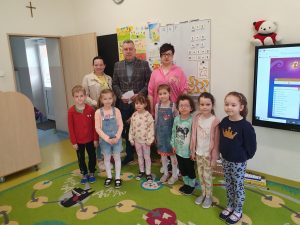Uczniowie oddziału przedszkolnego pozują do wspólnego zdjęcia wraz z przedstawicielami Rady Rodziców. Dzieci stoją w jednym rzędzie przed trojgiem dorosłych.