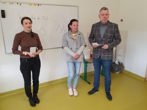 Dwoje przedstawicieli Rady Rodziców pozuje do wspólnego zdjęcia wraz z wychowawczynią klasy pierwszej. Zarówno wychowawczyni jak i przewodniczący klasy trzymają w dłoniach koperty.