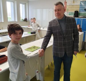 Przewodniczący Rady Rodziców ściska dłoń skarbnikowi klasy szóstej. Chłopiec patrzy w stronę obiektywu, a przewodniczący na niego.